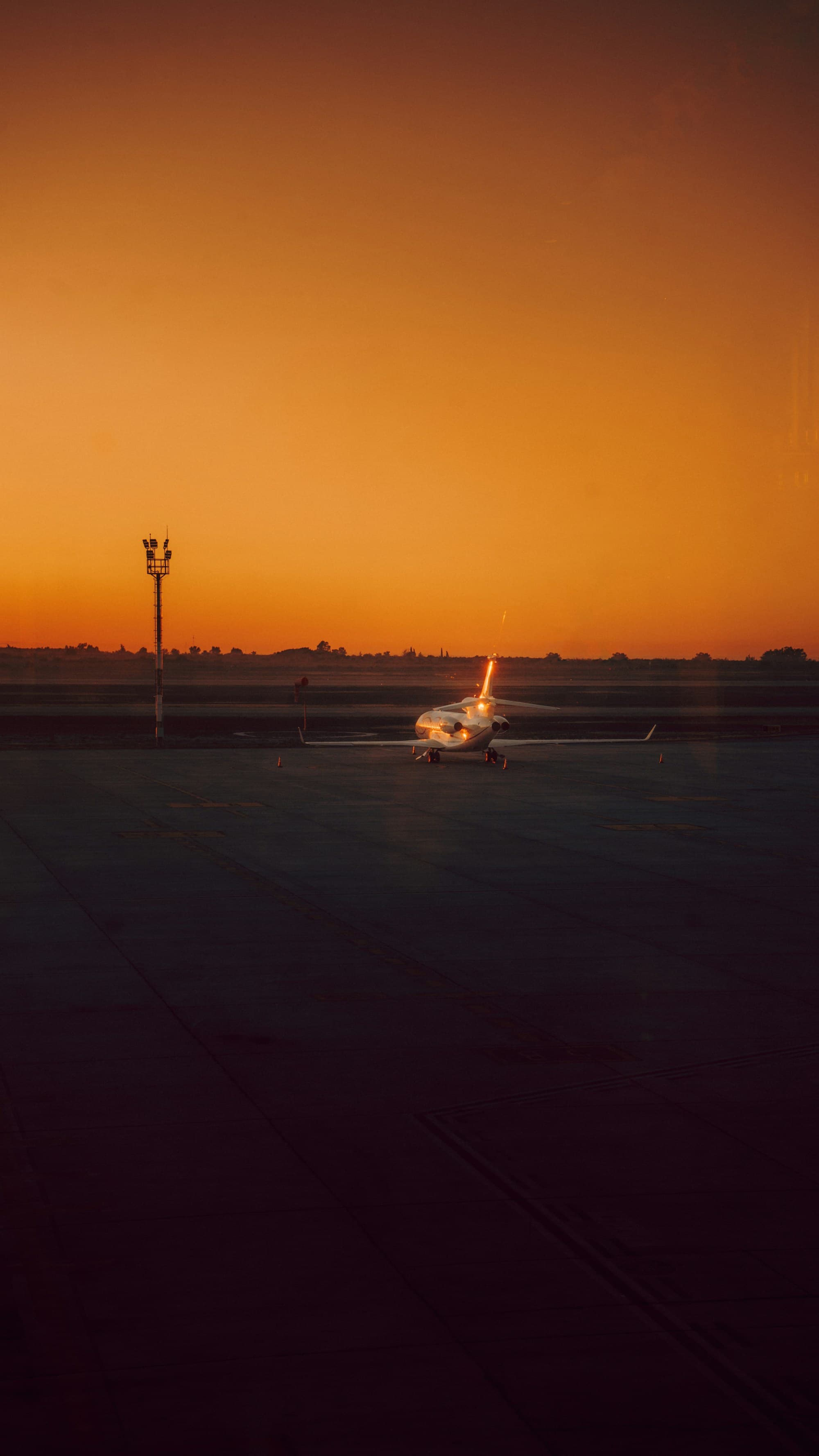 Private jet alone on the tarmac under an orange sunset sky, tail number toward the light